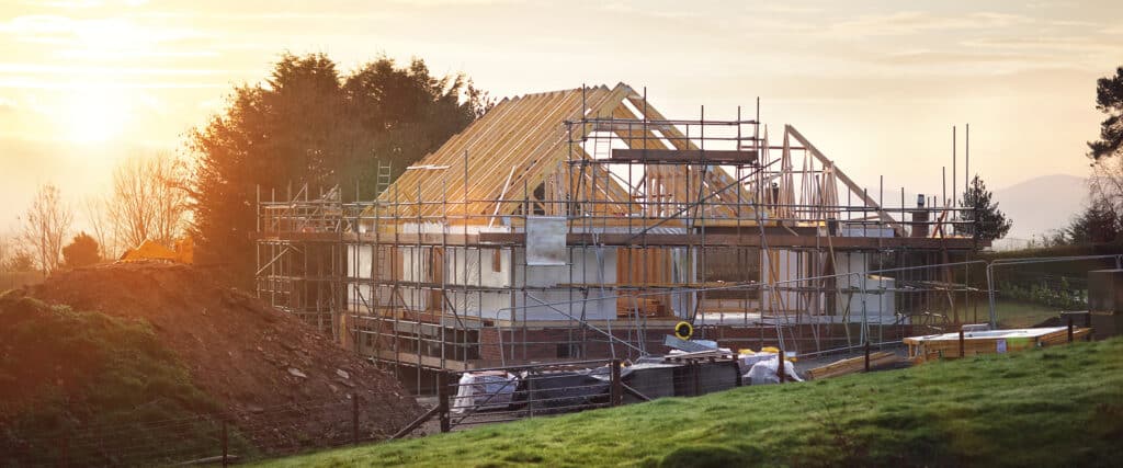 Chantier de construction d'une maison avec ossature bois et échafaudage, sous un soleil couchant. Excavateur et matériaux.